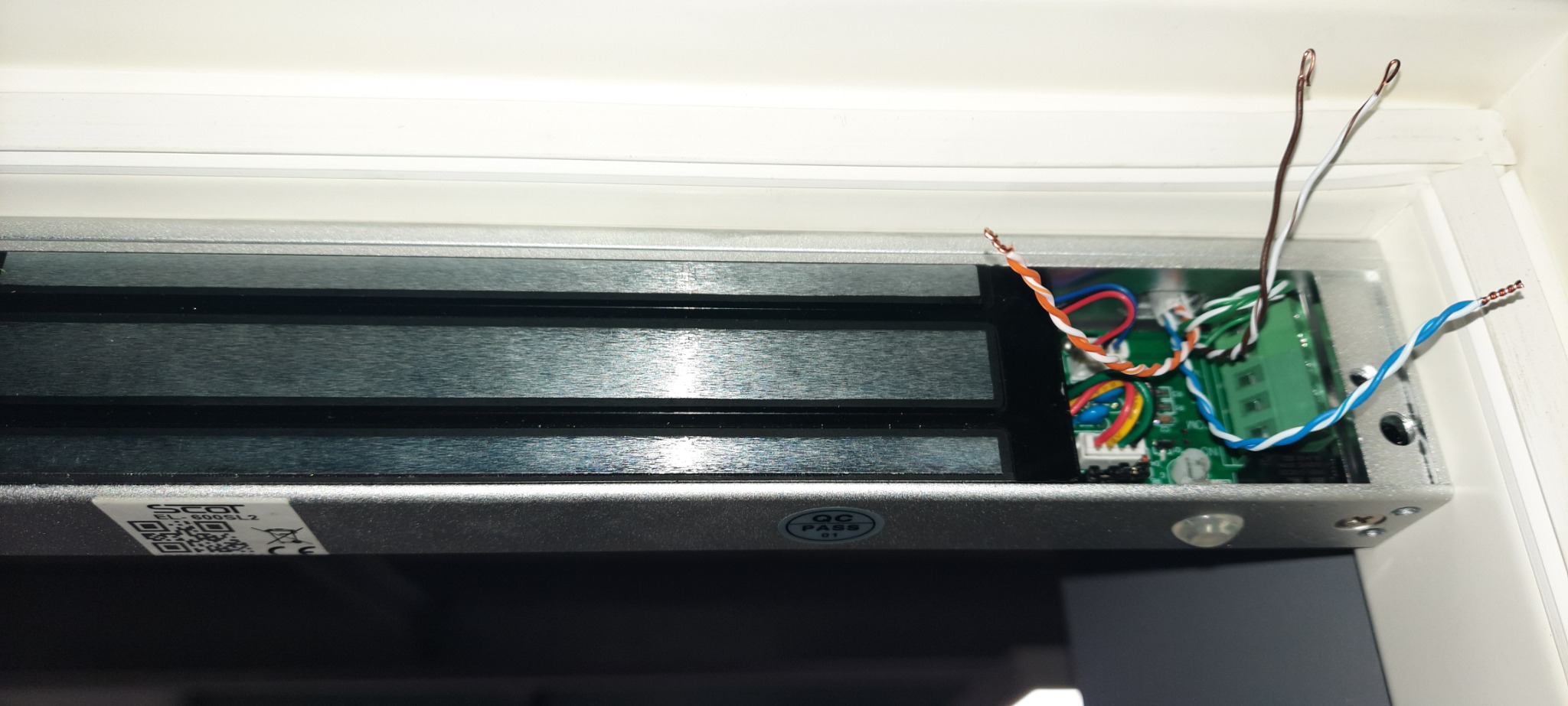 Elektromagnetyczny zamek do drzwi z widoczną elektroniką i przewodami podczas instalacji w ościeżnicy.