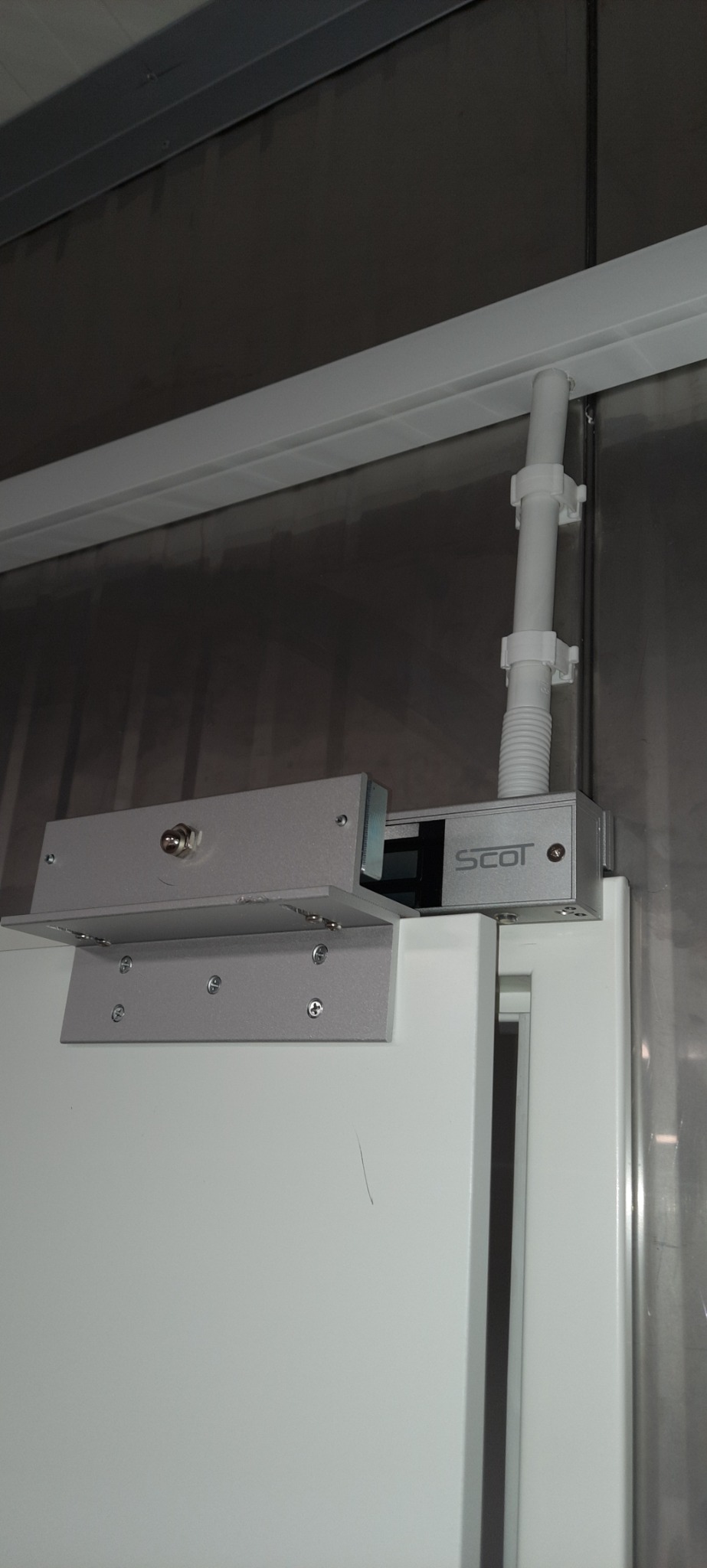 Elektromagnetyczny zamek SCOT zamontowany na białych drzwiach w Katowicach, widoczne przewody w białej rurce przymocowanej do sufitu.