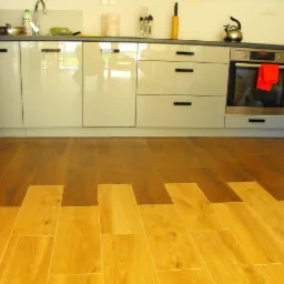 Wykończona podłoga w kuchni z płytek imitujących drewno, ułożonych w geometryczny wzór, na tle jasnych szafek kuchennych i sprzętów.
