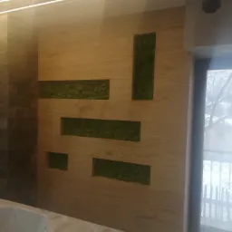 Nowoczesna łazienka z drewnianą ścianą z wnękami wypełnionymi zielonym mchem, obok ściana z kamienia i fragment wanny, za oknem zimowy krajobraz.