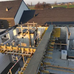 Budowa domu w trakcie wylewania stropu, widoczne szalunki i zbrojenie, w tle domy jednorodzinne.