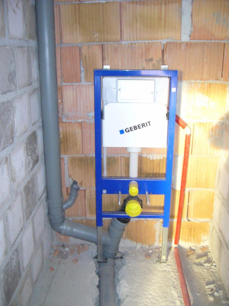 Stelaż podtynkowy Geberit zamontowany w surowym stanie, widoczne rury kanalizacyjne i instalacja wodna w ścianie z cegły.