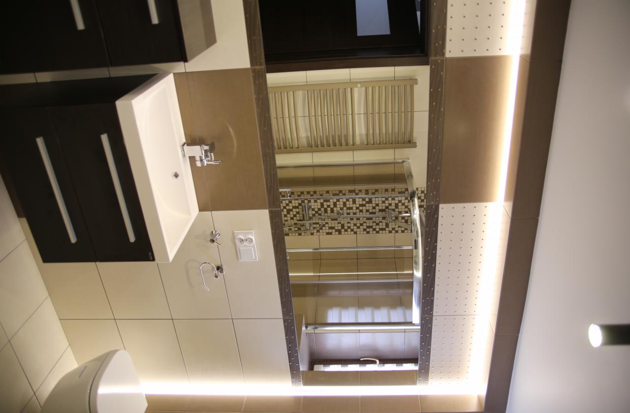 Nowoczesna łazienka po remoncie: umywalka z szafką, lustro z oświetleniem LED, beżowe płytki i dekoracyjna mozaika. Widok z dołu do góry.