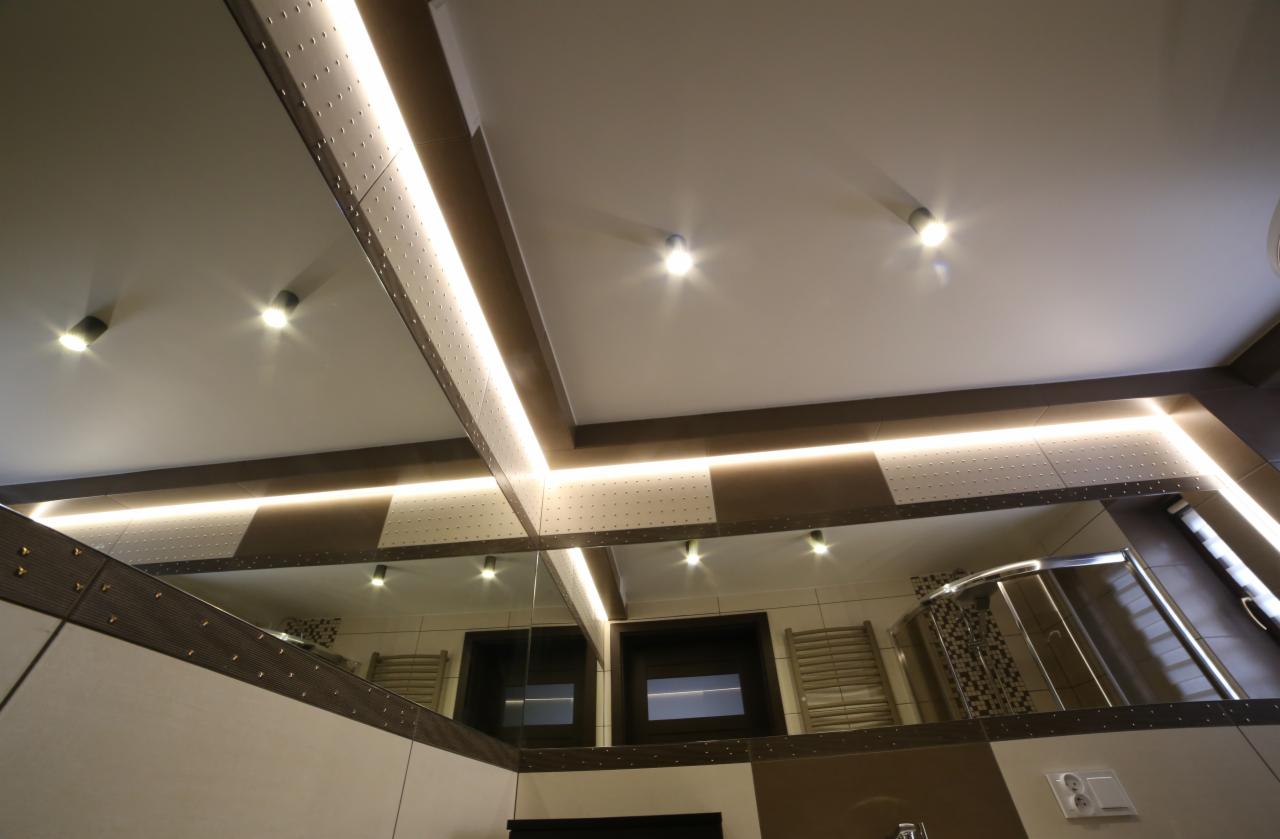 Nowoczesna łazienka z podświetlanym sufitem i lustrem odbijającym kabinę prysznicową. Nietypowe wykończenie sufitu z elementami dekoracyjnymi.