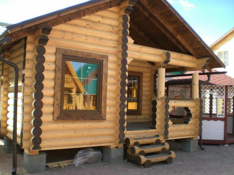 Niewielki domek z okrągłych bali sosnowych z zadaszonym wejściem, widoczne schody z bali i ozdobne wykończenia wokół okien.