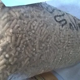 Worek wypełniony pelletem drzewnym, widoczne granulki w przezroczystym opakowaniu, etykieta na spodzie worka. Ujęcie z góry pod kątem.