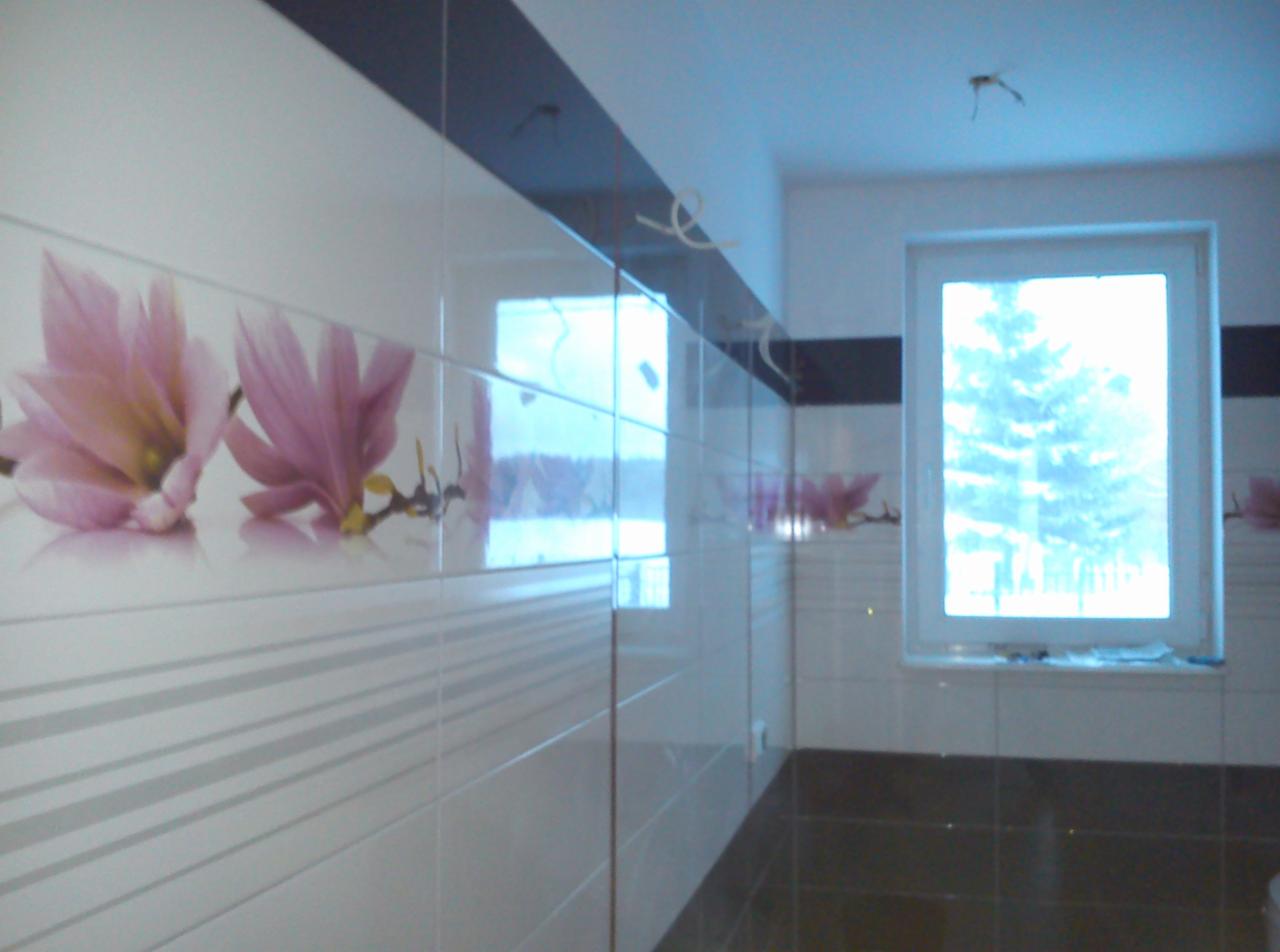 Wykończona łazienka z białymi płytkami z motywem różowych kwiatów i ciemną podłogą, widok na okno z zimowym krajobrazem.