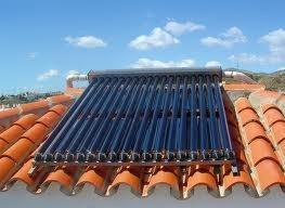 Kolektory słoneczne rurowe zamontowane na pomarańczowej dachówce, widoczne niebieskie niebo z chmurami w tle.