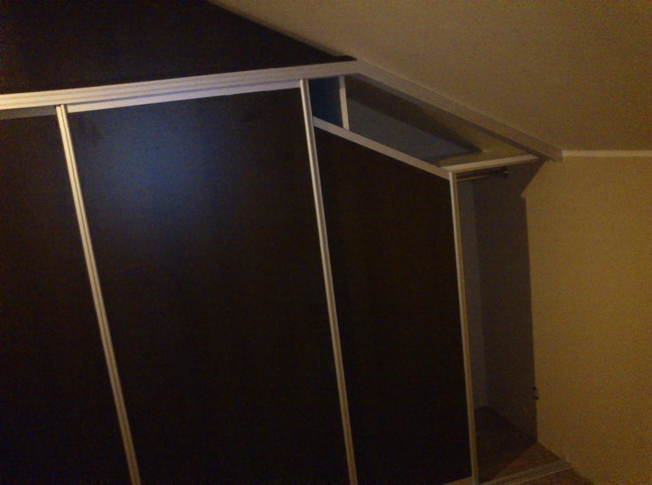 Ciemna szafa wnękowa z przesuwnymi drzwiami i aluminiowymi ramami, widok z dołu, oświetlenie wnętrza szafy widoczne przy otwartej części.