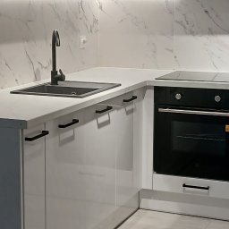 Daniel Grela - Nowoczesna, biała kuchnia z czarną armaturą i marmurowym backsplashiem podświetlonym LED, prezentująca minimalistyczny design i funkcjonalność.