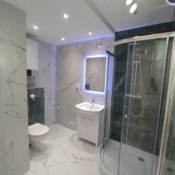 Daniel Grela - Elegancka łazienka po remoncie z marmurowymi płytkami, kabiną prysznicową i podświetlanym lustrem. Nowoczesne oświetlenie sufitowe.