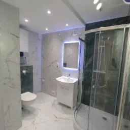 Elegancka łazienka po remoncie z marmurowymi płytkami, kabiną prysznicową i podświetlanym lustrem. Nowoczesne oświetlenie sufitowe.