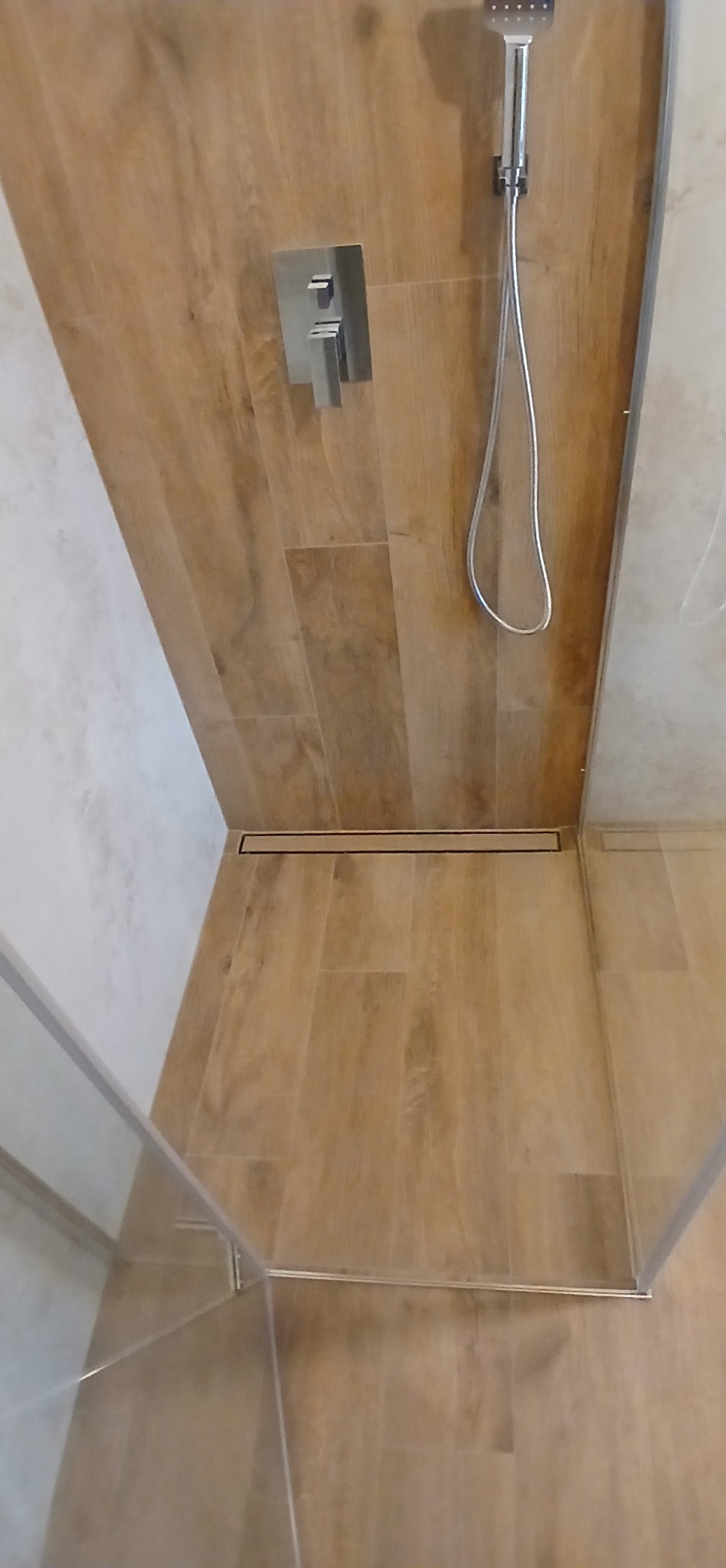 Nowoczesna kabina prysznicowa z drewnopodobnymi płytkami, minimalistyczną armaturą i odpływem liniowym. Widok z góry, ukazujący detale wykończenia.