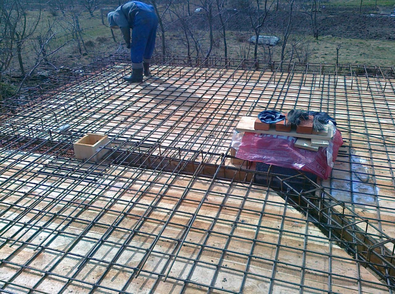 Zbrojenie stropu na deskowaniu z widocznym pracownikiem w kombinezonie. Na zbrojeniu cegły i narzędzia. Widok z góry na konstrukcję szkieletową.