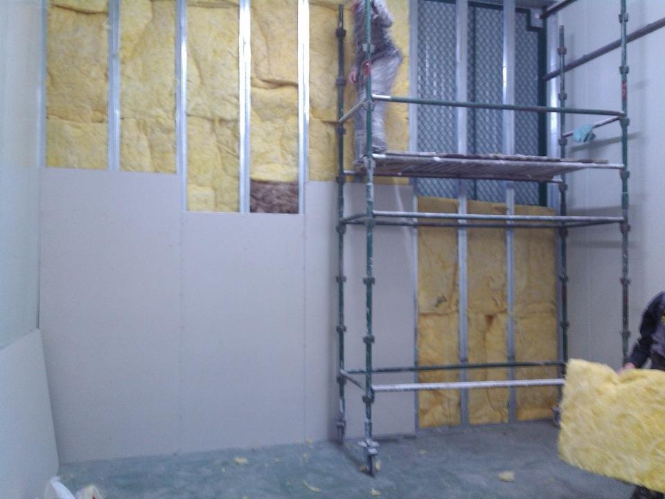 Ocieplanie ścian wełną mineralną i montaż płyt karton-gips w Bolszewie. Prace na rusztowaniu, widoczna konstrukcja metalowa i izolacja termiczna.