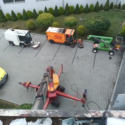 Usługi Wysokościowe FHU Mix Bud Piotr Smagacz - Widok z góry na parking z kilkoma pojazdami specjalistycznymi, w tym na podnośnik koszowy z pracownikiem w niebieskiej czapce, obok zadbane trawniki i drzewa.