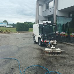 Usługi Wysokościowe FHU Mix Bud Piotr Smagacz - Maszyna CMAR LC580 w trakcie czyszczenia mokrej kostki brukowej przed budynkiem, widoczny niebieski wąż doprowadzający wodę.