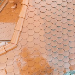 Usługi Wysokościowe FHU Mix Bud Piotr Smagacz - Nowy dach z okrągłą dachówką ceramiczną w odcieniach brązu, z widocznym systemem rynnowym. Dachówka lekko połyskuje, sugerując świeże malowanie lub impregnację.