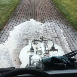 Usługi Wysokościowe FHU Mix Bud Piotr Smagacz - Maszyna czyszcząca kostkę brukową w trakcie pracy, widok z perspektywy operatora, część kostki już umyta, w tle trawnik.