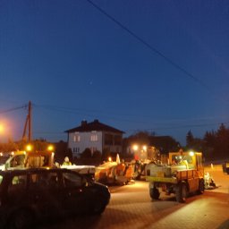 Usługi Wysokościowe FHU Mix Bud Piotr Smagacz - Pojazdy służb drogowych ustawione na kostce brukowej o zmierzchu, z zapalonymi światłami ostrzegawczymi i roboczymi, w tle widoczny dom jednorodzinny.