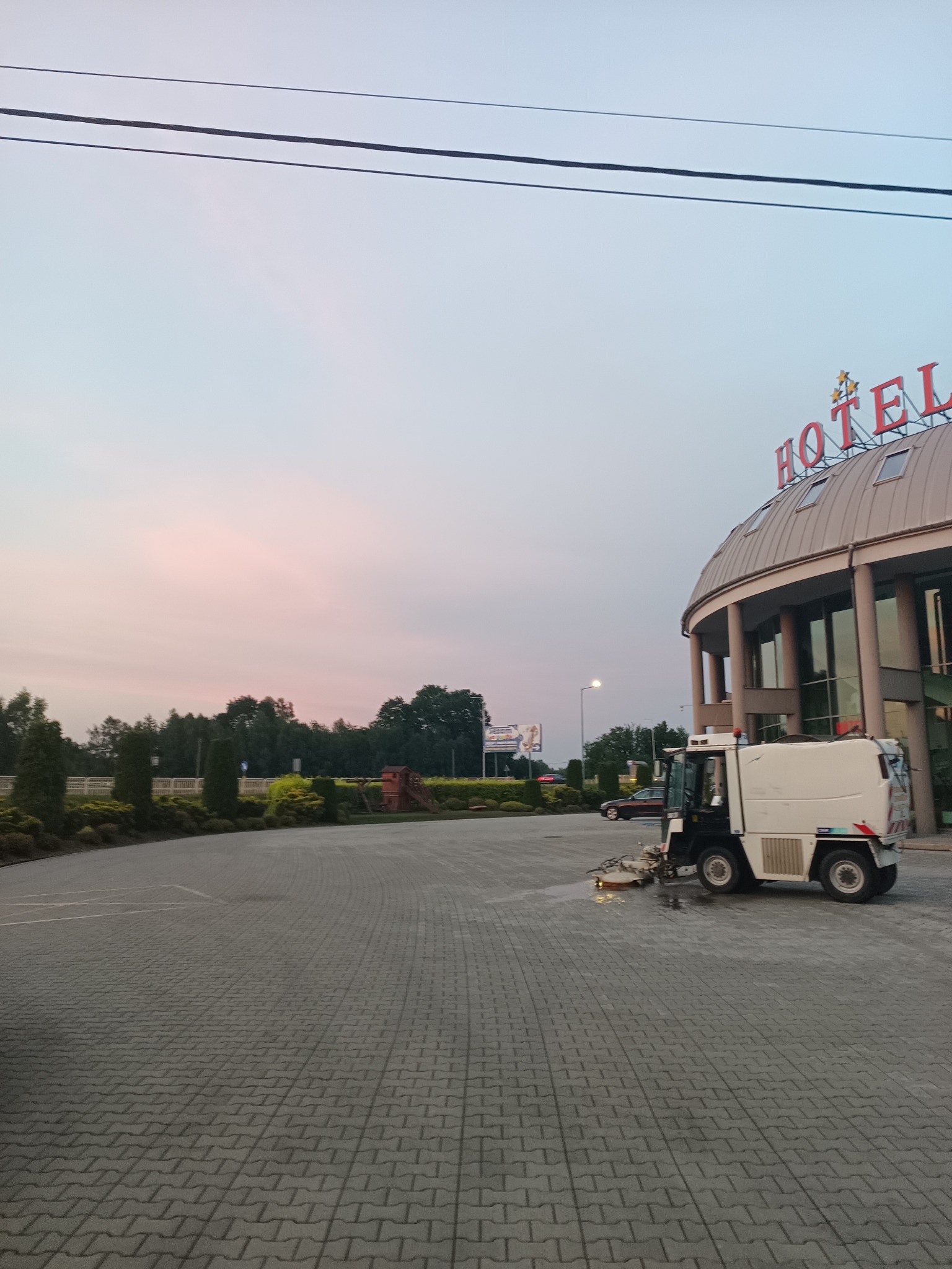 Maszyna czyszcząca na kostce brukowej przed hotelem o zmierzchu.