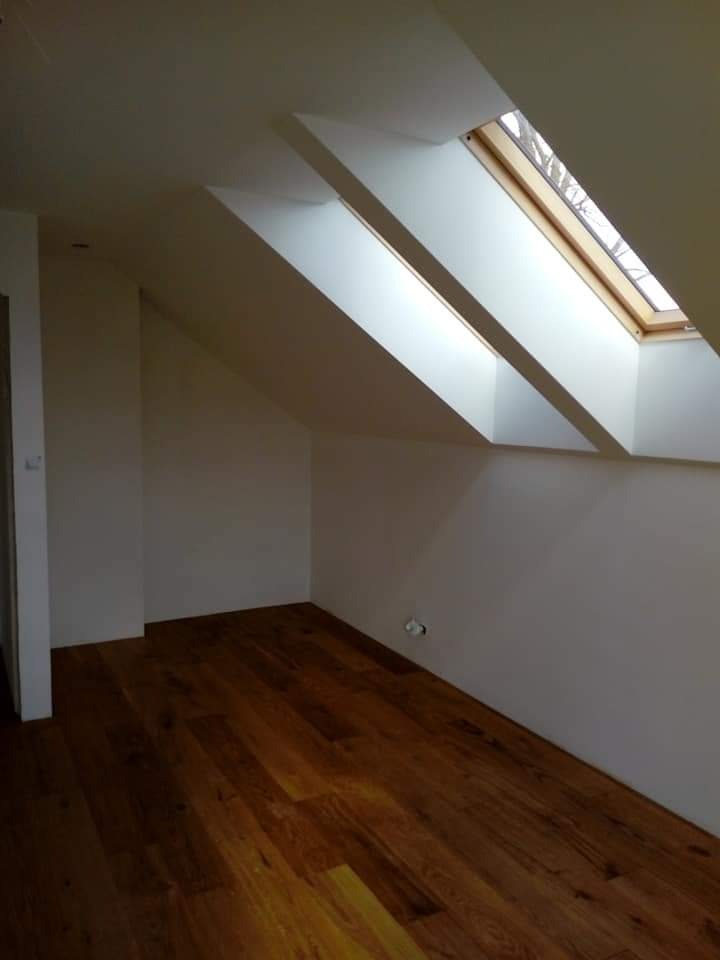 Poddasze z drewnianą podłogą i dwoma oknami dachowymi w drewnianych ramach, pomalowane na biało.