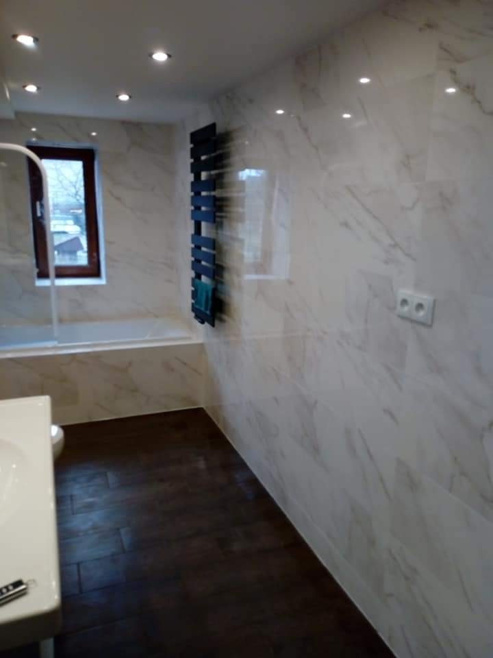 Wykończona łazienka w Mszczonowie z marmurowymi płytkami na ścianach, ciemną drewnianą podłogą, grzejnikiem drabinkowym i nowoczesną armaturą.