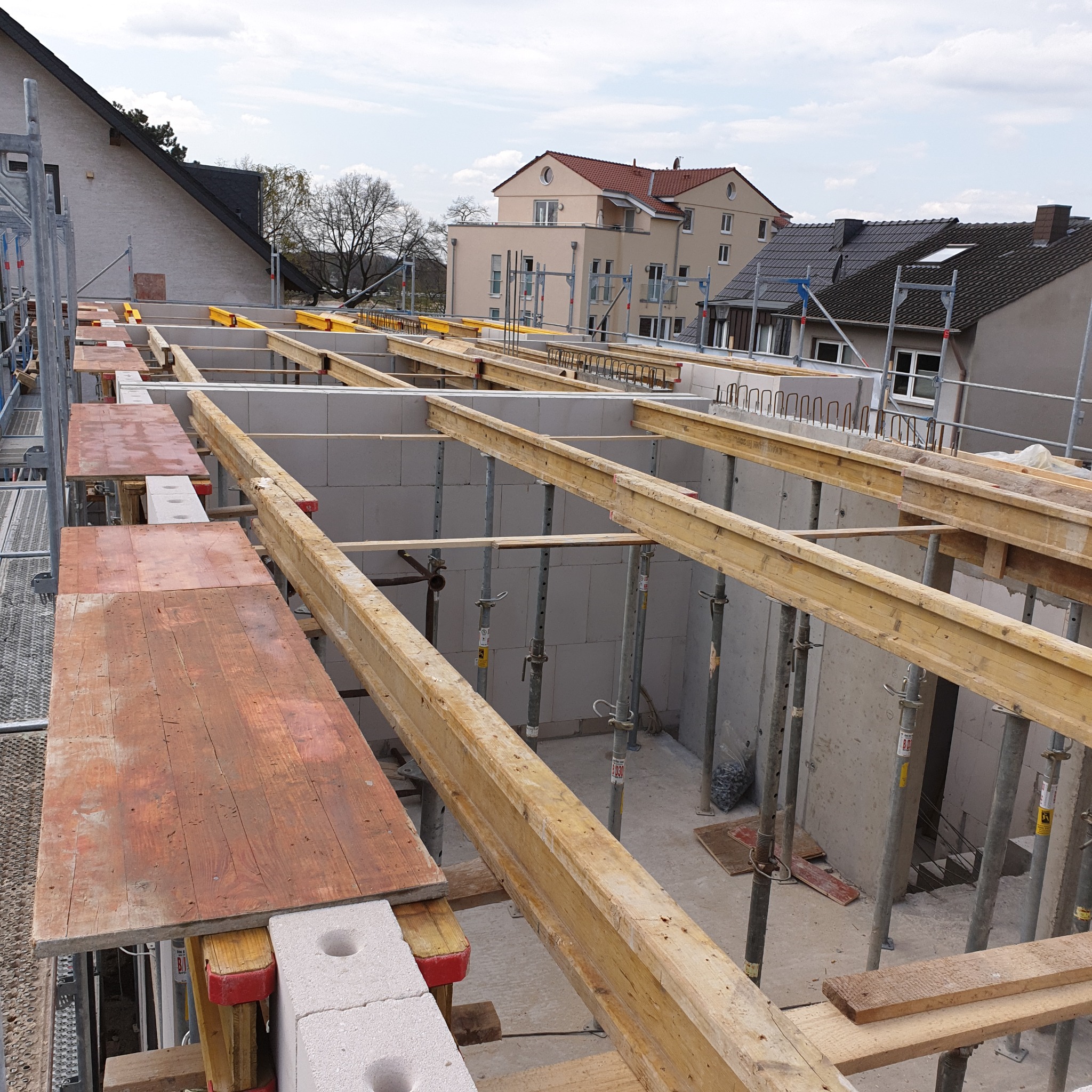 Wznoszenie ścian z bloczków betonu komórkowego Ytong, widoczne drewniane stemple podtrzymujące strop, rusztowanie i okoliczna zabudowa w tle.