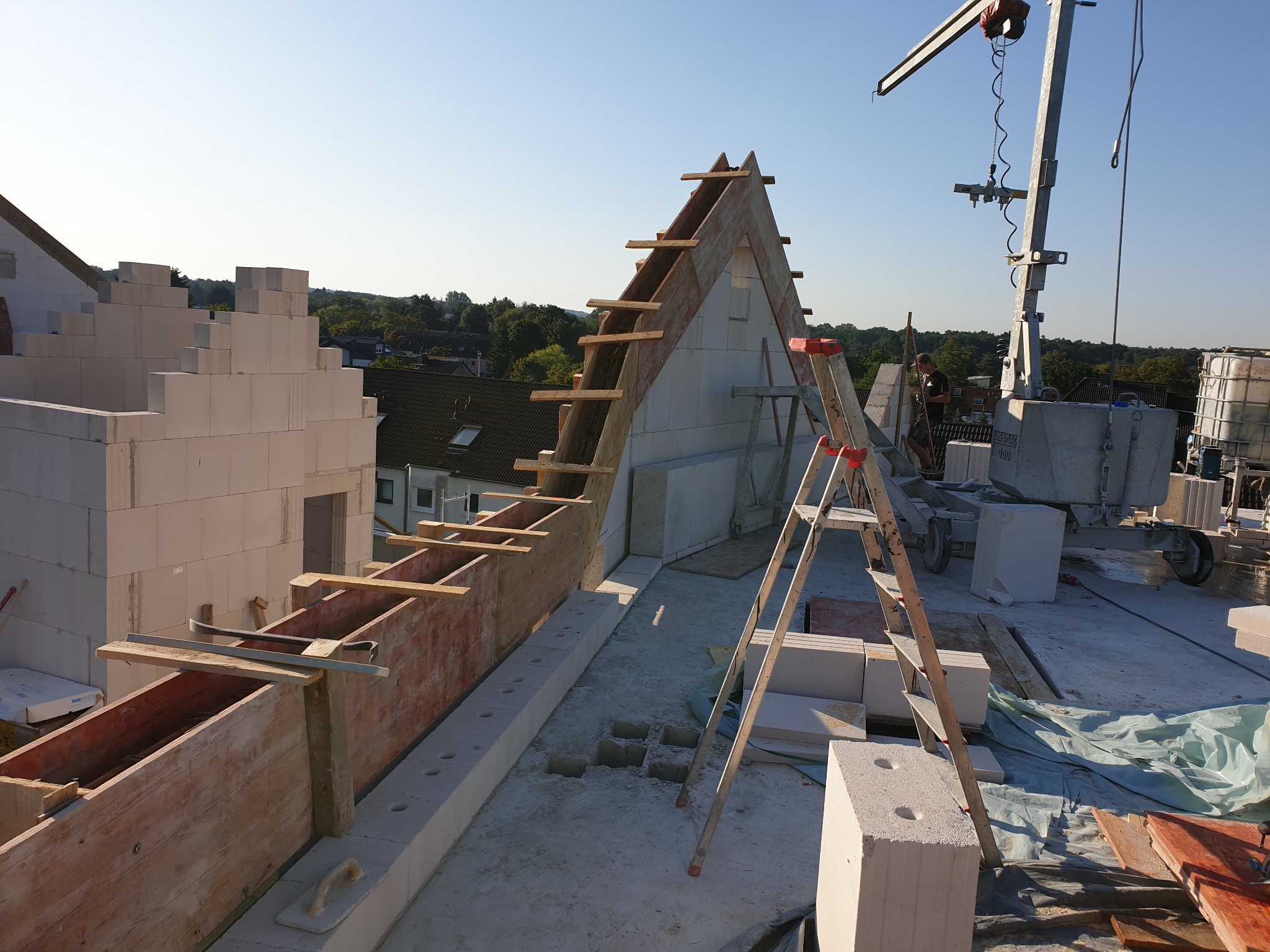 Wznoszenie ścian szczytowych z bloczków betonu komórkowego na budowie domu, widoczny dźwig, drewniane szalunki i drabina.