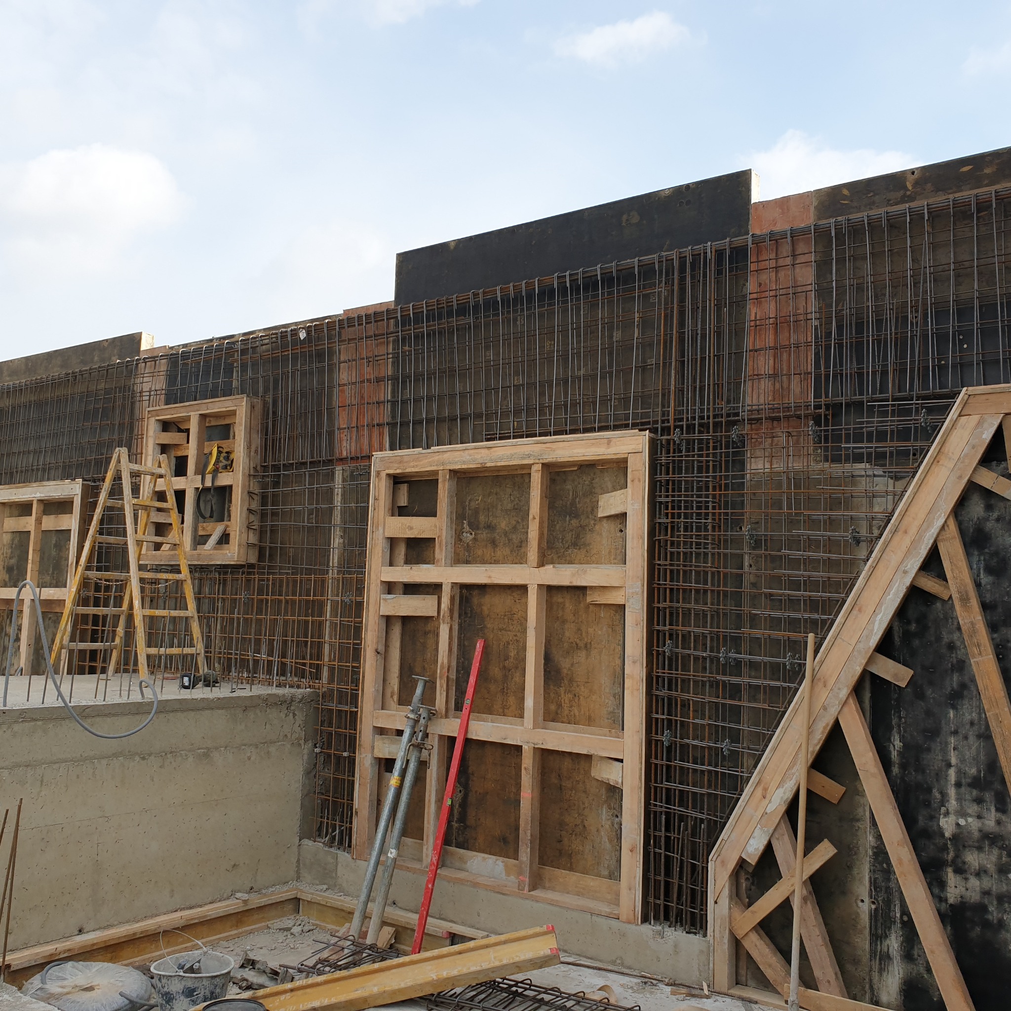 Szczegółowy widok szalunków i zbrojenia pod wylewkę fundamentów domu murowanego, widoczne drewniane ramy, siatka zbrojeniowa i drabina oparta o konstrukcję.