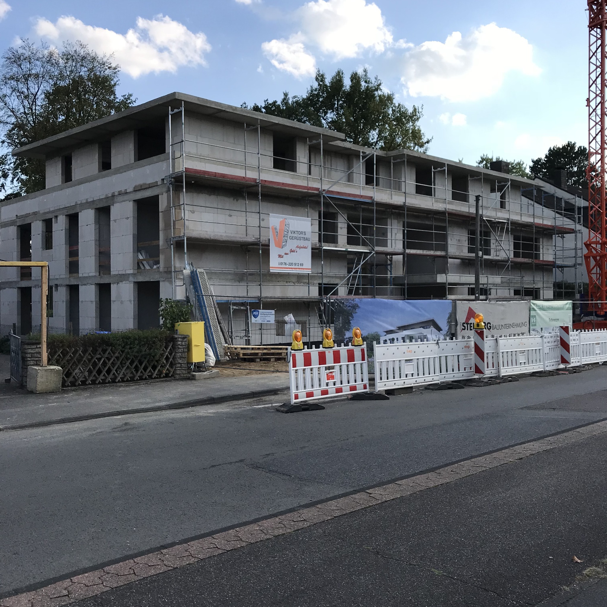 Surowy stan budynku wielorodzinnego z betonu komórkowego w trakcie budowy, z rusztowaniami i dźwigiem w tle, zabezpieczony barierkami z żółtymi lampami ostrzegawczymi.