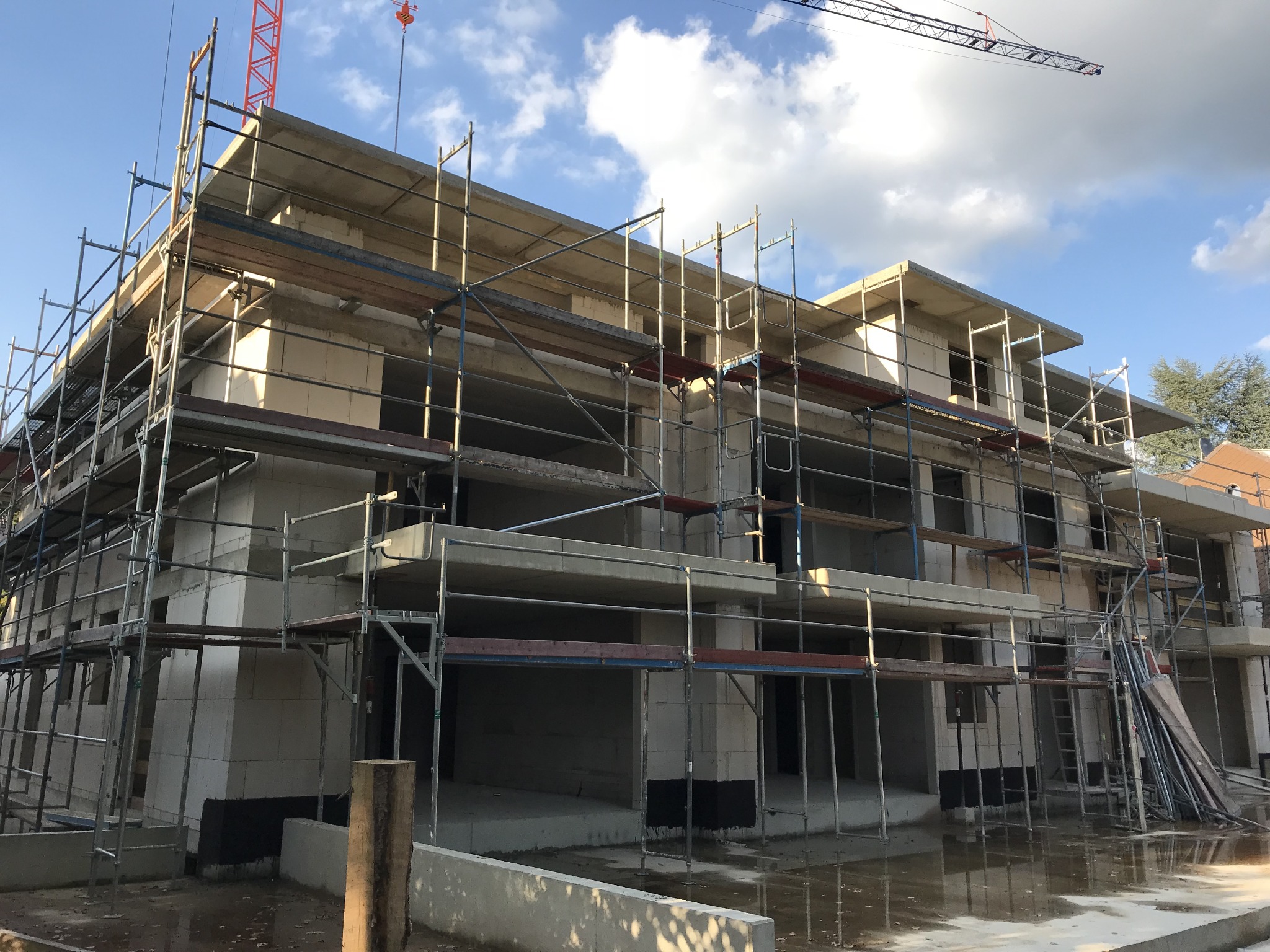 Wznoszenie ścian z betonu komórkowego na budowie trzypiętrowego domu w zabudowie szeregowej, widoczne rusztowania i dźwig w tle.