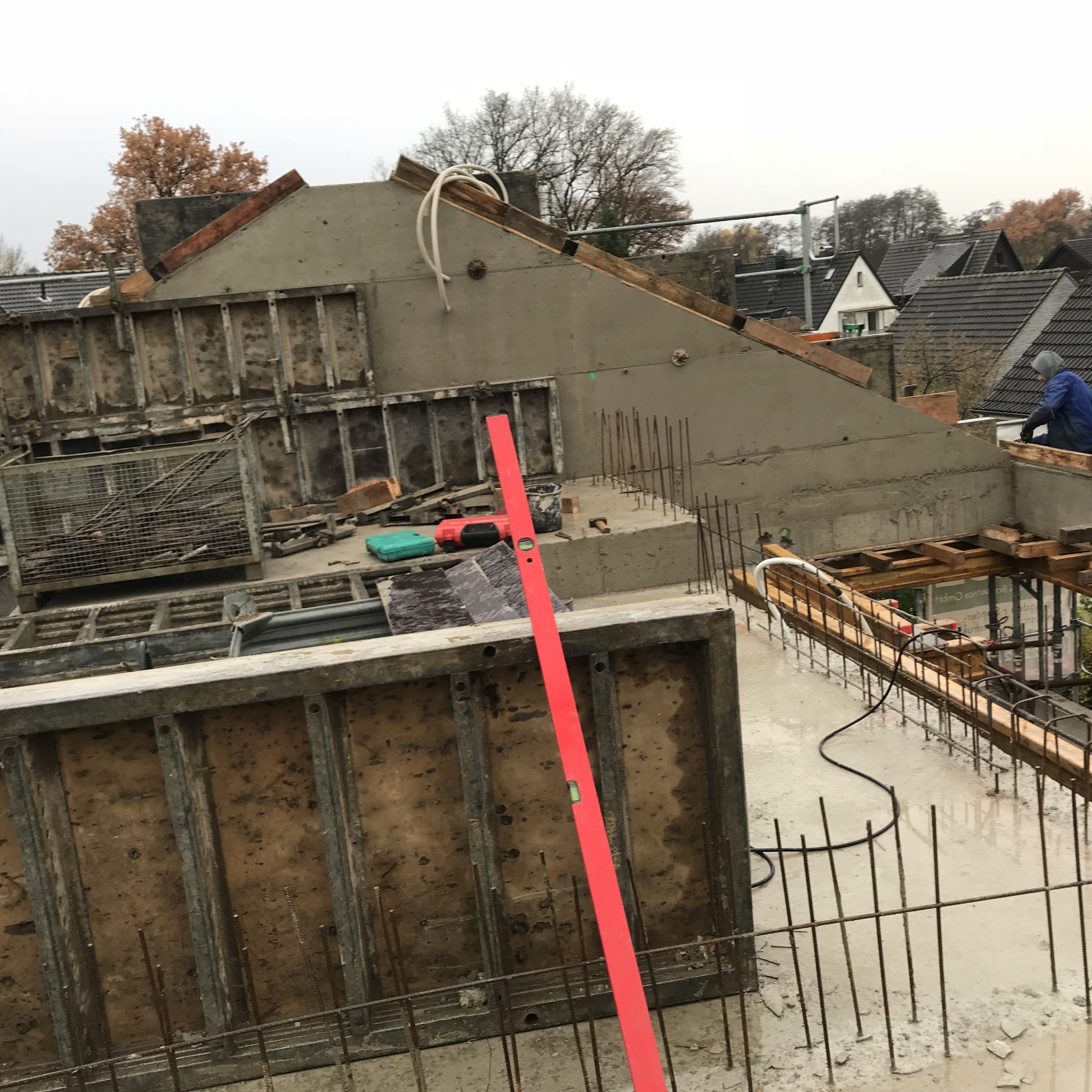 Wznoszenie betonowej konstrukcji zbrojonej na dachu budynku w trakcie rozbudowy, widoczny poziomica, narzędzia i pracownik w tle.