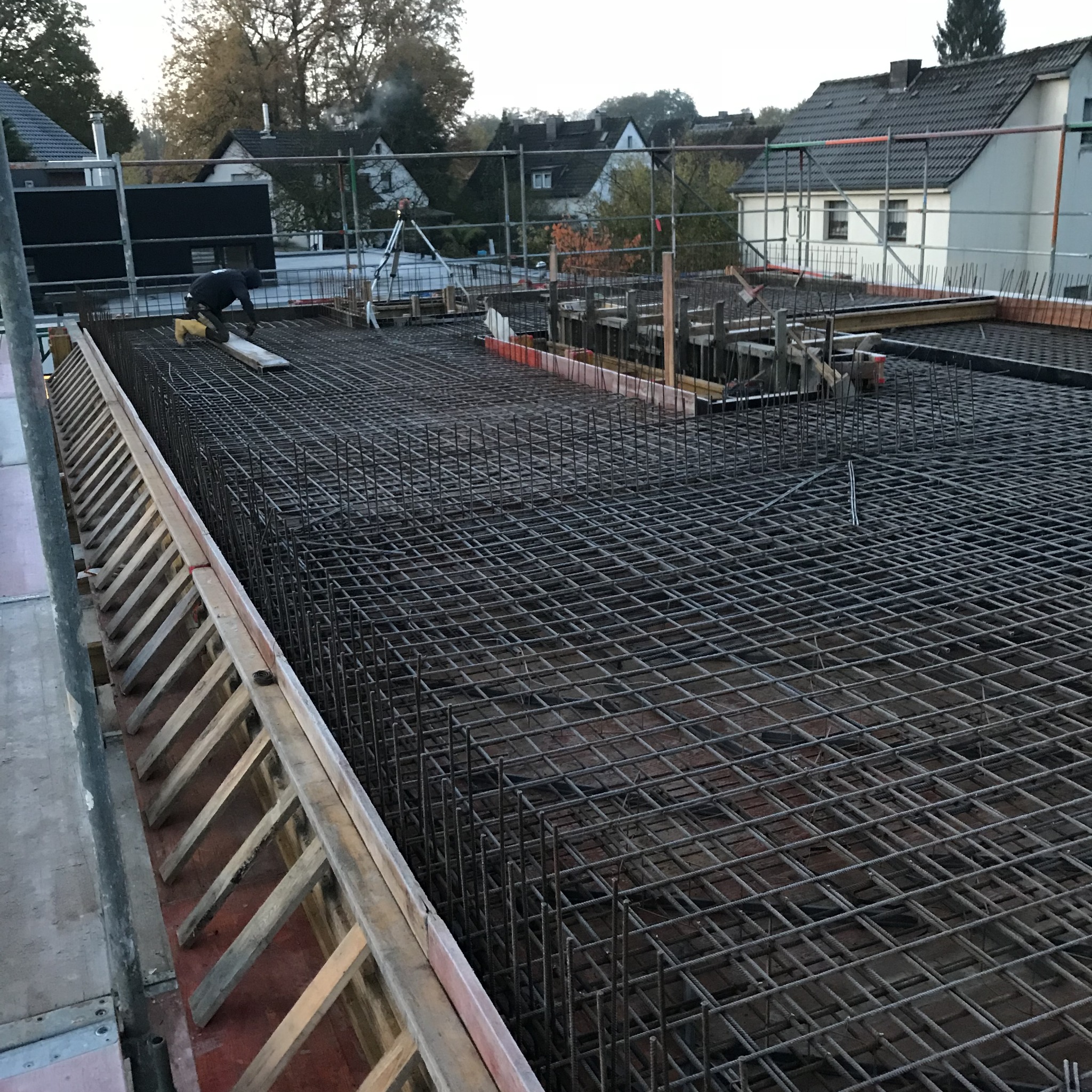 Zbrojenie płyty fundamentowej na budowie domu jednorodzinnego, widoczne rusztowania i pracownik w oddali.