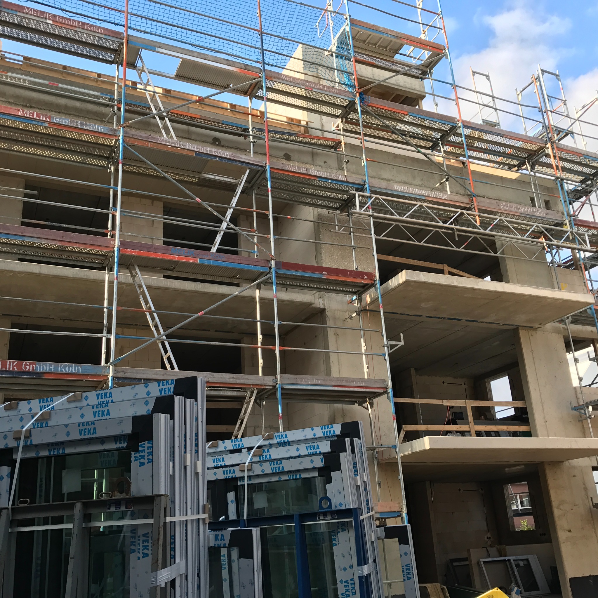 Surowy stan domu w trakcie budowy, z widocznymi rusztowaniami i oknami VEKA czekającymi na montaż.