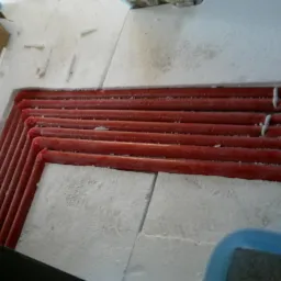 Czerwone rury ogrzewania podłogowego ułożone w izolacji ze styropianu, widok z góry. Fragment instalacji przed zalaniem posadzki.