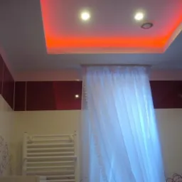 Łazienka z podwieszanym sufitem z czerwonym podświetleniem LED, białe płytki z fioletowymi wzorami i bordowe pasy na ścianach, biała zasłonka i grzejnik.