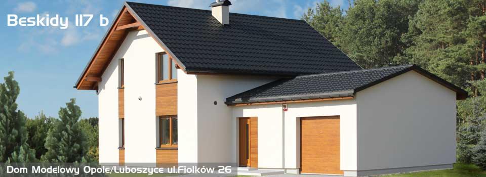 Elewacja domu z garażem w stylu nowoczesnym. Białe ściany, drewniane akcenty, ciemna dachówka. Widoczne drzewa w tle. Dom modelowy Beskidy 117b.