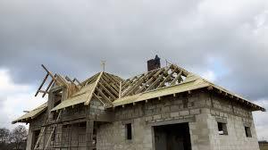 Budowa dachu na domu jednorodzinnym w Dopiewie, widoczne krokwie i deski, stan surowy otwarty, pochmurne niebo w tle.