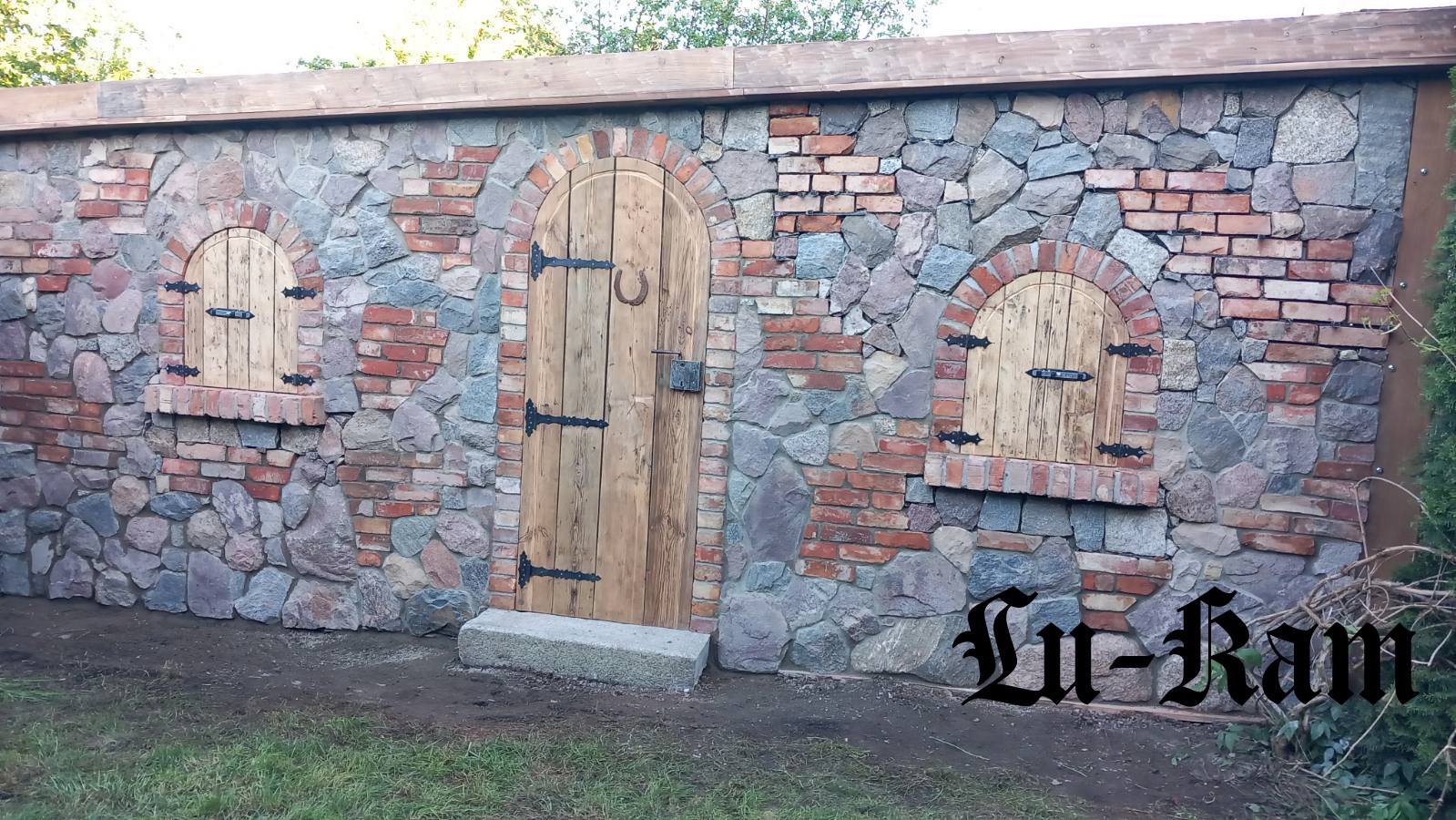 Kamienno-ceglana ściana z drewnianymi elementami: łukowe okienka z okiennicami i drzwi z podkową. Nietypowe połączenie materiałów i rustykalny styl.