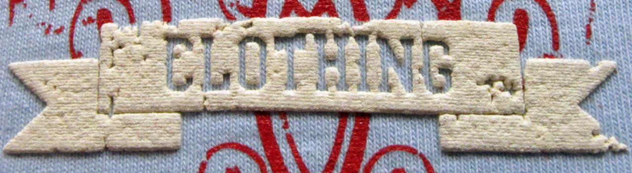 Close-up of a textured, off-white banner-shaped patch with cut-out lettering spelling CLOTHING, sewn onto a light blue knitted fabric with red decorative elements.