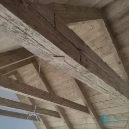 Drewniana konstrukcja dachu z widocznymi belkami i deskowaniem, surowy stan wykończenia, widok z dołu.