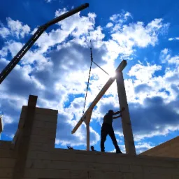 Sylwetka pracownika montującego drewnianą konstrukcję domu z bali przy pomocy dźwigu na tle błękitnego nieba z chmurami.