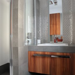 Pracownia na nowo - Nowoczesna łazienka z kabiną prysznicową za szkłem, umywalką na szafce z drewnianym frontem i mozaiką na ścianie. Minimalistyczny design, szare płytki i chromowane detale.