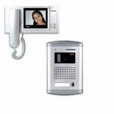 Zestaw wideodomofonowy: panel zewnętrzny w kolorze srebrnym z kamerą i głośnikiem oraz biały monitor wewnętrzny z wyświetlaczem prezentującym twarz kobiety.