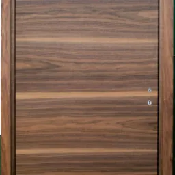 Drewniane drzwi z widocznym usłojeniem, dwa otwory na klamkę i zamek, prosty design.