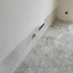 Przygotowanie do osuszania ścian: widoczne otwory wentylacyjne i instalacja elektryczna w surowym, szarym pomieszczeniu z betonową podłogą.