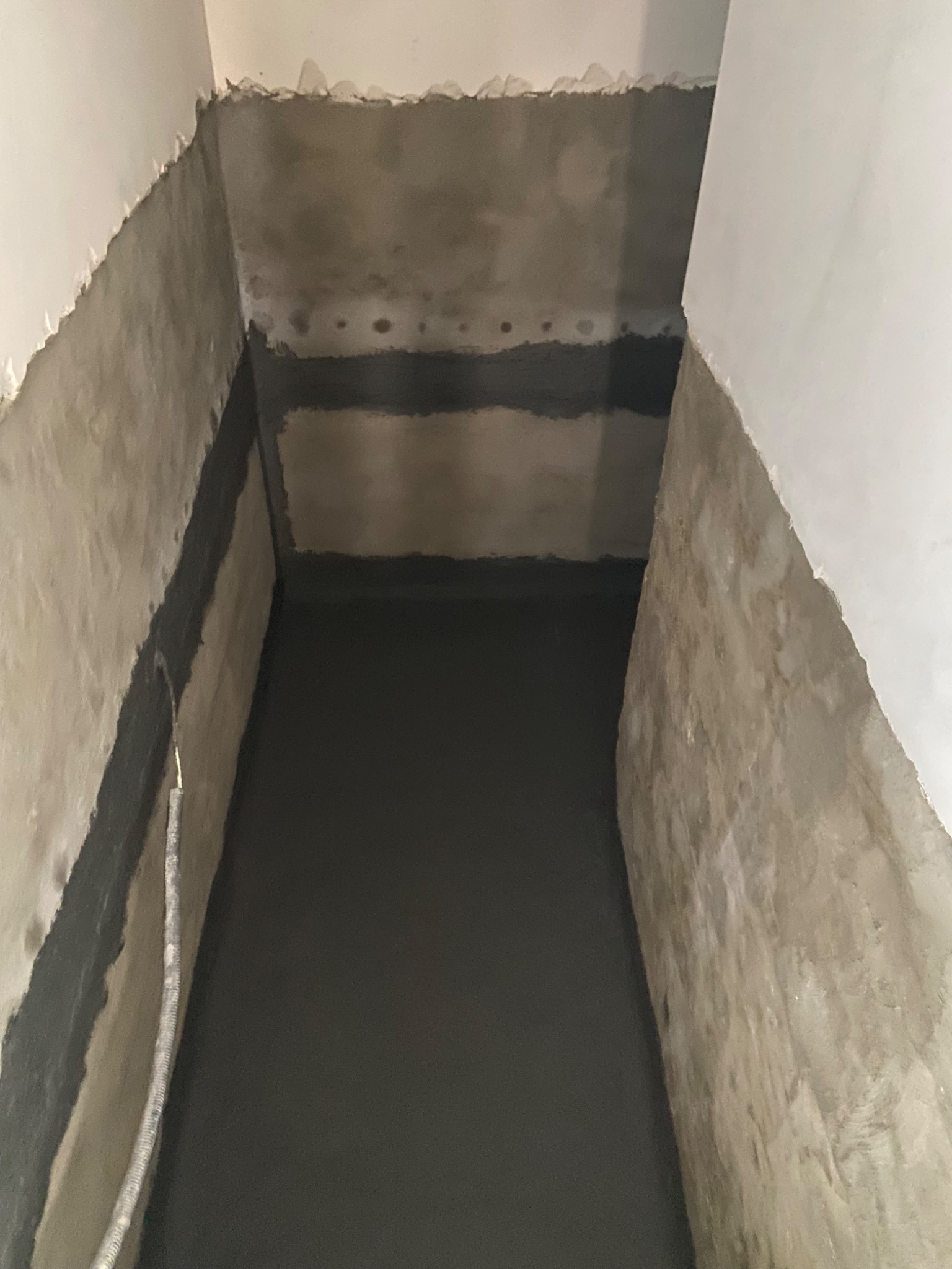 Świeżo zaizolowany fundament w Łodzi, z widocznymi warstwami hydroizolacji na ścianach i podłodze. Szare ściany i podłoże, widoczne ślady po uszczelnieniach.