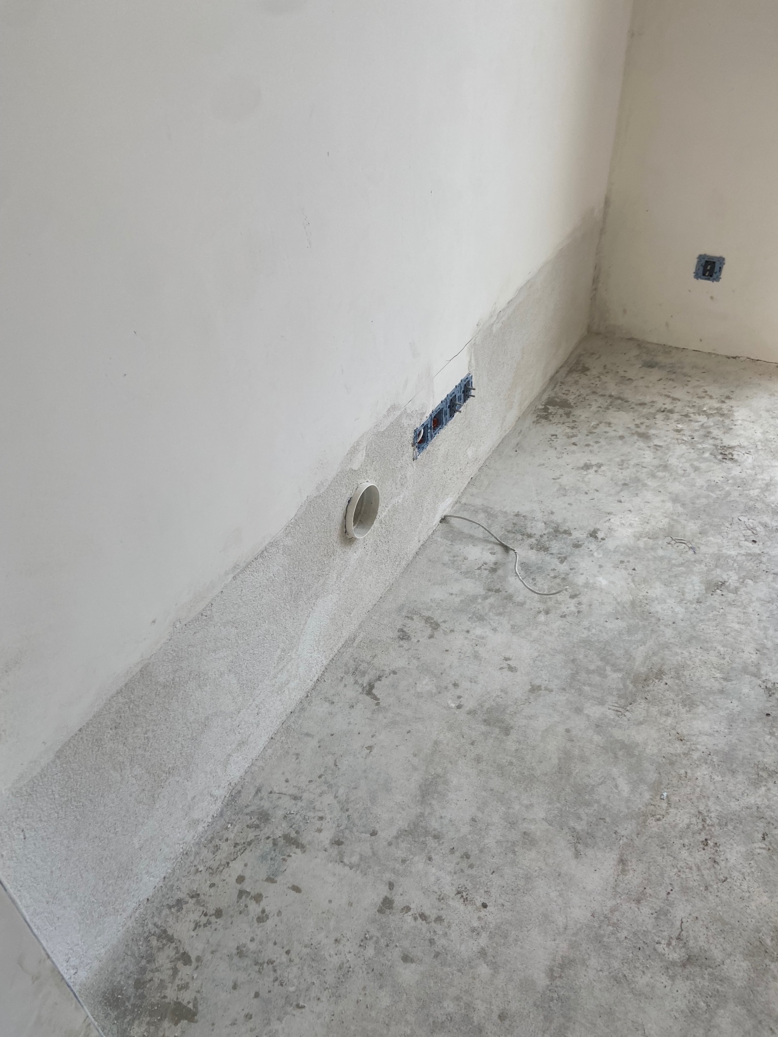 Przygotowanie do osuszania ścian: widoczne otwory wentylacyjne i instalacja elektryczna w surowym, szarym pomieszczeniu z betonową podłogą.