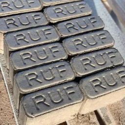 Ułożone na drewnianej palecie, szare brykiety RUF z widocznym odciśniętym napisem, uchwycone w naturalnym świetle słonecznym.